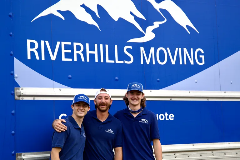 Three RiverHills movers in branded polos and caps beside the blue moving truck